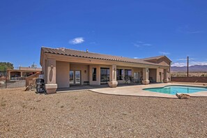 A two-story building with a swimming pool, outdoor seating, and a mountainous backdrop.
