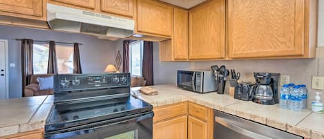 A compact kitchen with wooden cabinets, a built-in stove, a microwave, and a coffee maker.