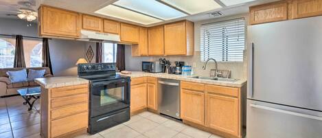 Cocina compacta con armarios de madera, refrigerador de acero inoxidable, lavavajillas y estufa negra.
