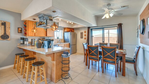 A kitchen with a central island, bar stools, a dining area with chairs, a ceiling fan, and a large window.