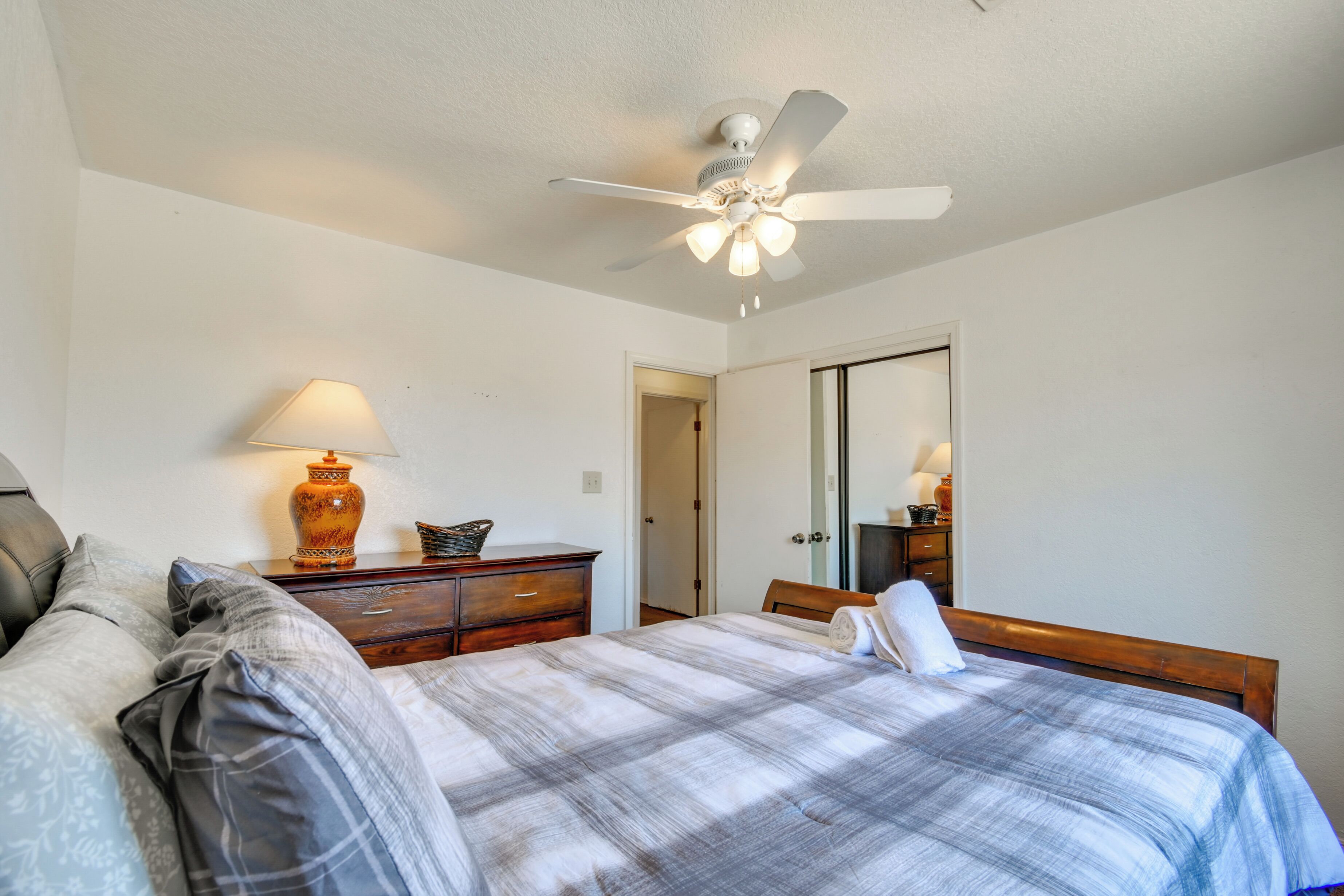 A bedroom with a bed, a nightstand, a lamp, a ceiling fan, a dresser, and a mirror.