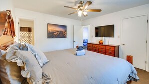 A bedroom with a large bed, a ceiling fan, a TV, and a painting on the wall.