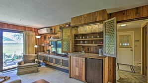 A kitchen with wooden cabinets, a built-in bar, and a large window overlooking a grassy area. - 3 Mi to Silver Lake: Traverse City Home w/ Deck (Traverse City)