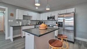 A modern kitchen with white cabinets, a stainless steel refrigerator, and a central island with stools. - Peaceful Apache Junction Condo ~ 1 Mi to Downtown! (Apache Junction)