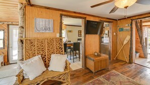 L’intérieur d’un chalet rustique, avec un mur en bois, un lit doté d’une tête de lit en osier, un ventilateur de plafond et un téléviseur.