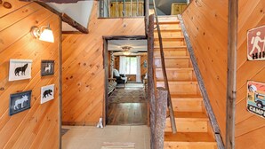 Un intérieur en bois avec un escalier menant à un deuxième étage, des murs en bois et une enseigne indiquant un campement.