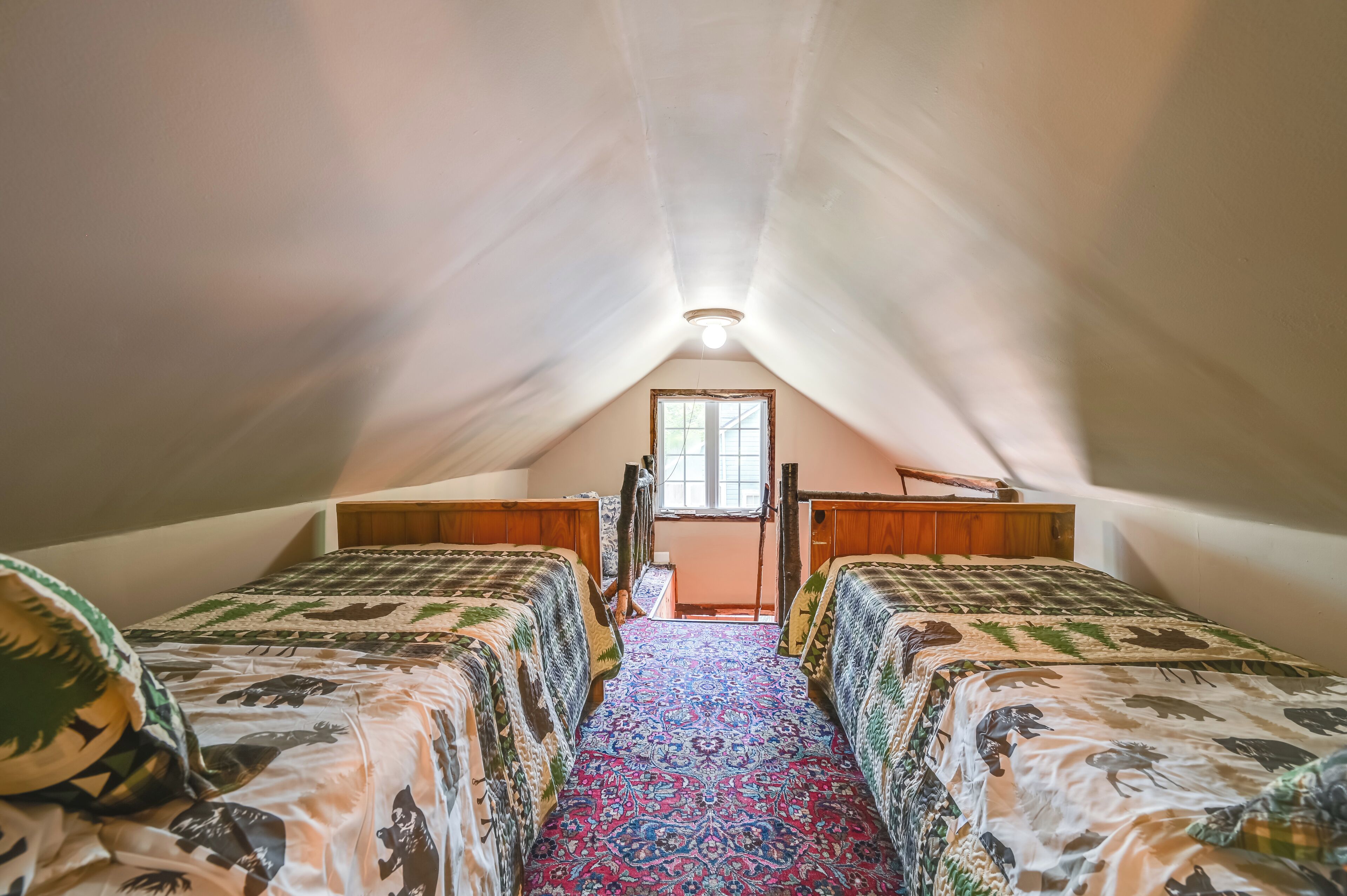 An attic bedroom with two beds, a wooden wardrobe, and a window.