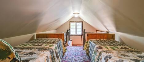 An attic bedroom with two beds, a wooden wardrobe, and a window.