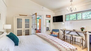 A bedroom with a bed, a desk with two chairs, a TV, and a window with a view of trees.