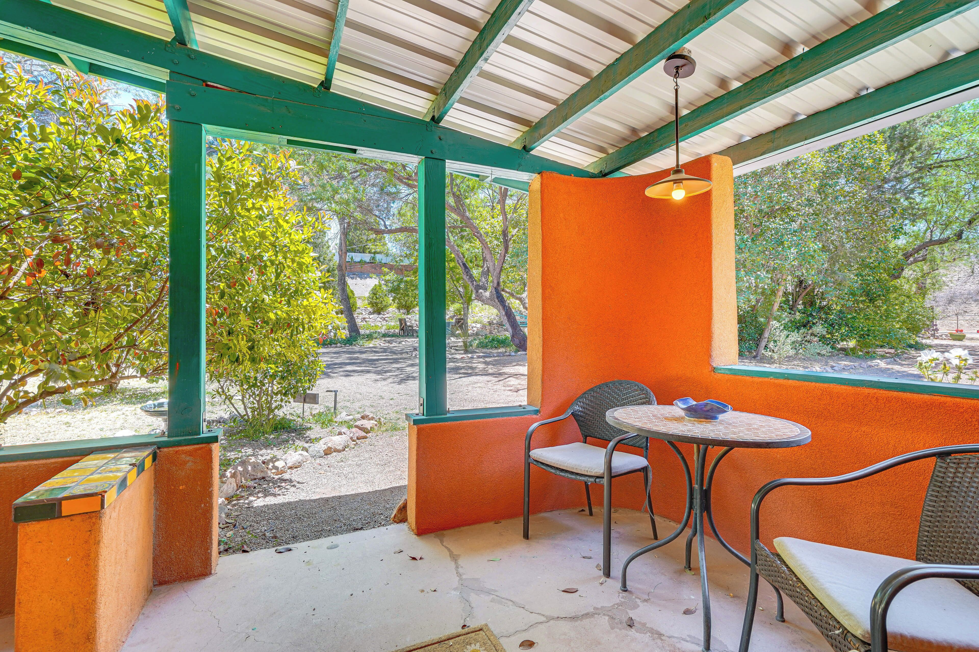 Un patio al aire libre con una mesa y sillas, rodeado de paredes anaranjadas y vigas estructurales verdes.