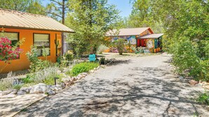 A rustic cabin with a gravel driveway, surrounded by lush greenery and cacti.