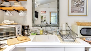 A kitchen with a white countertop, a stainless steel toaster, a coffee maker, a sink, and a hanging rack with cups.
