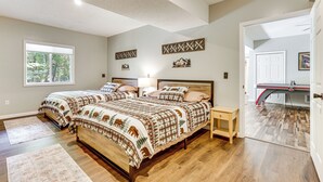 Een slaapkamer met twee bedden, een houten vloer, een raam en een deur die naar een andere kamer leidt.