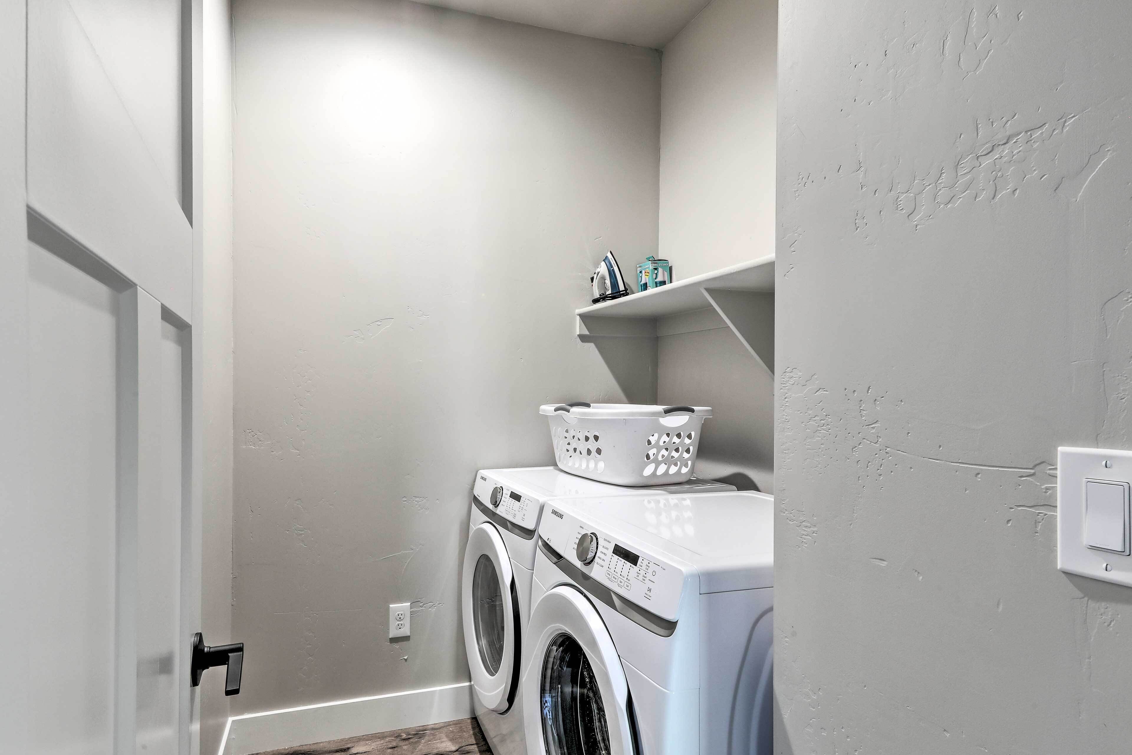 A laundry room with a washing machine and dryer, a basket on the dryer, and a shelf above holding laundry supplies.