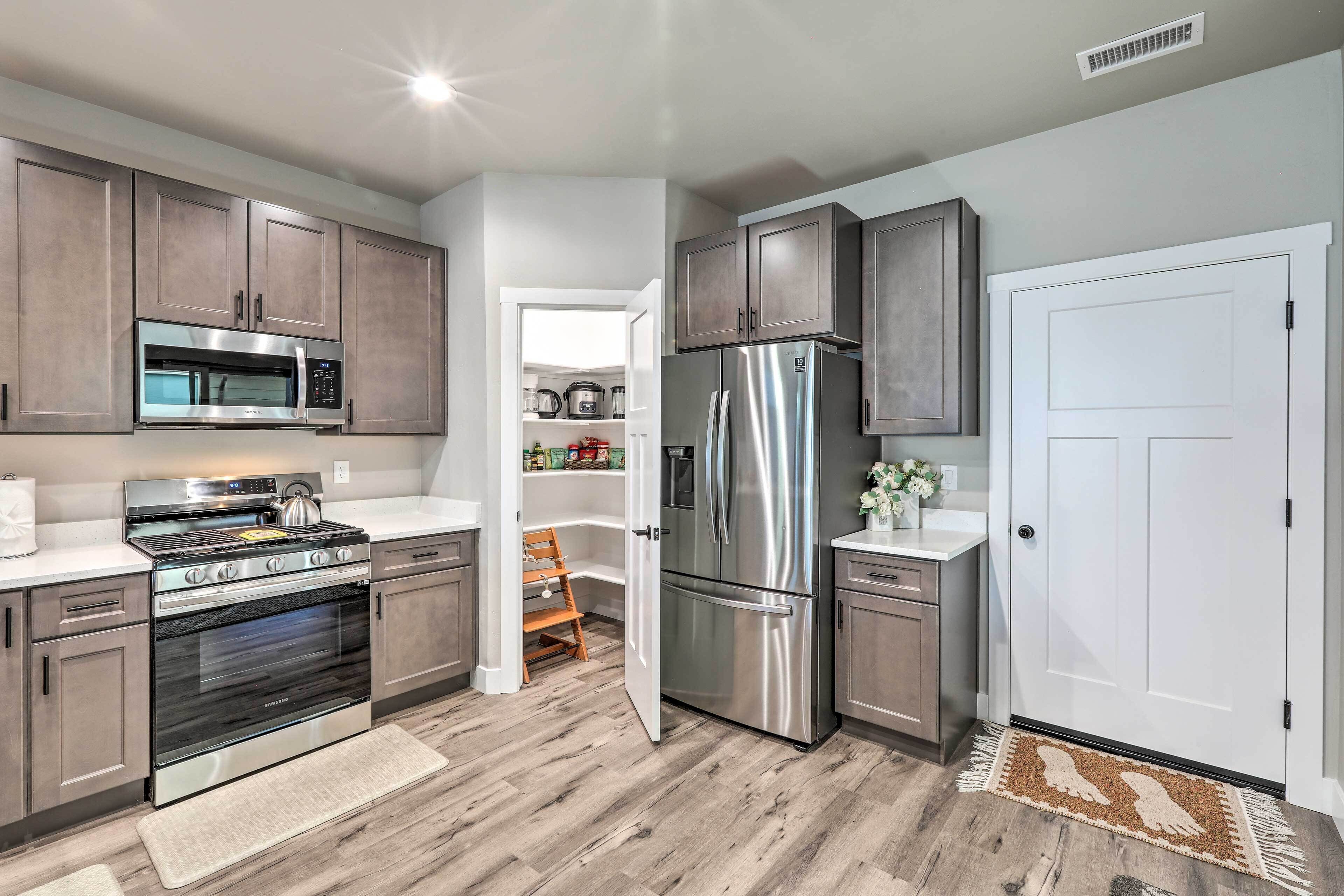 A modern kitchen with stainless steel appliances, wooden cabinets, and a white door.