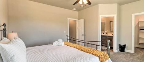 A bedroom with a bed, a ceiling fan, a bedside lamp, and a bathroom visible through an open door.