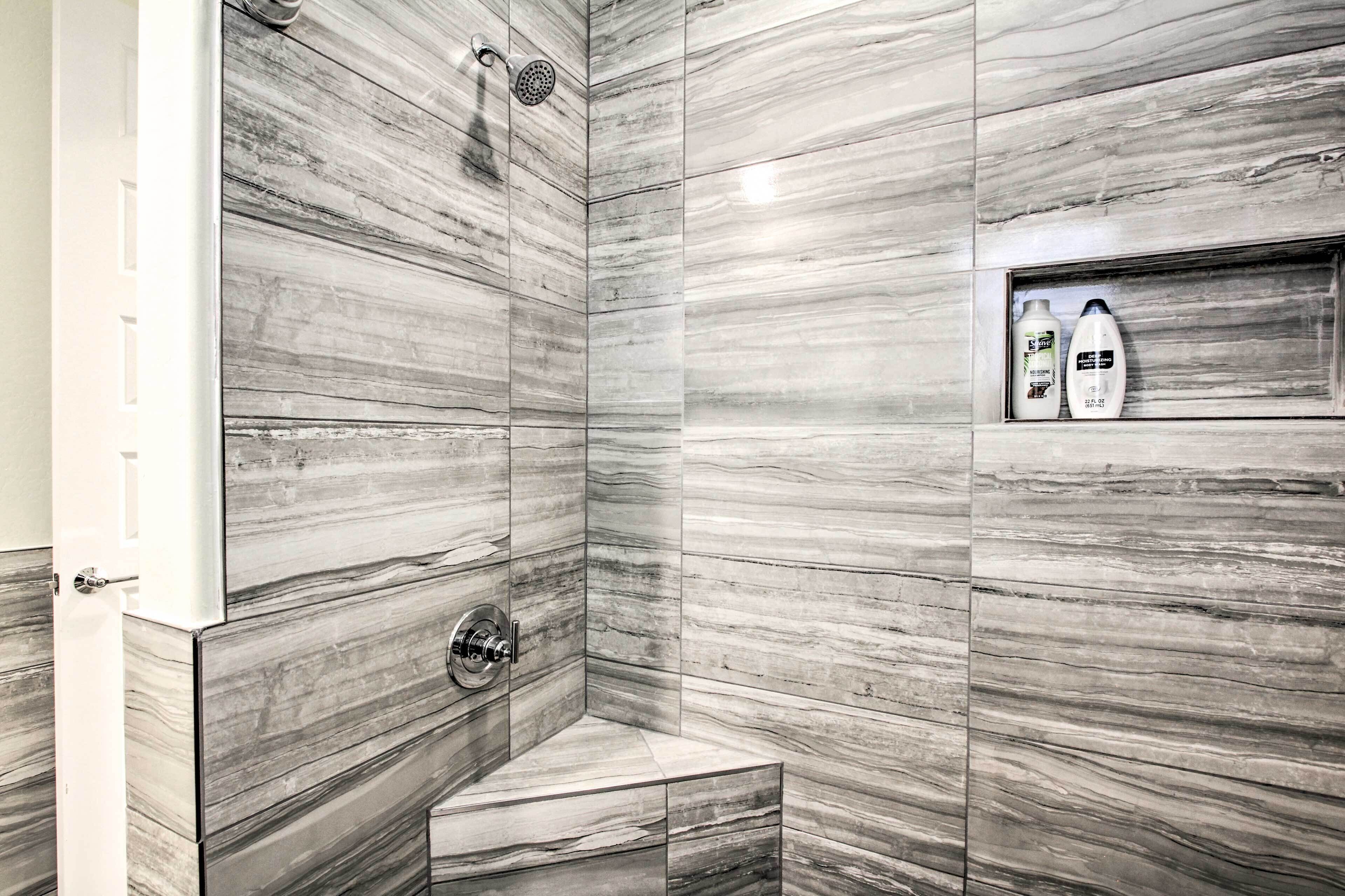 A modern bathroom with a shower, a built-in shelf with toiletries, and a marble wall design.