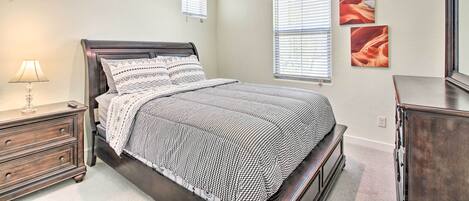 A bedroom with a bed, nightstand, dresser, and two windows with blinds.