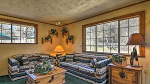 A cozy living room with a patterned sofa, a wooden coffee table, and a lamp. There are windows with plants on the windowsill and a view of the outdoors. - Lavish Sonora Suite on 10 Acres w/ Shared Pool! (Sonora)