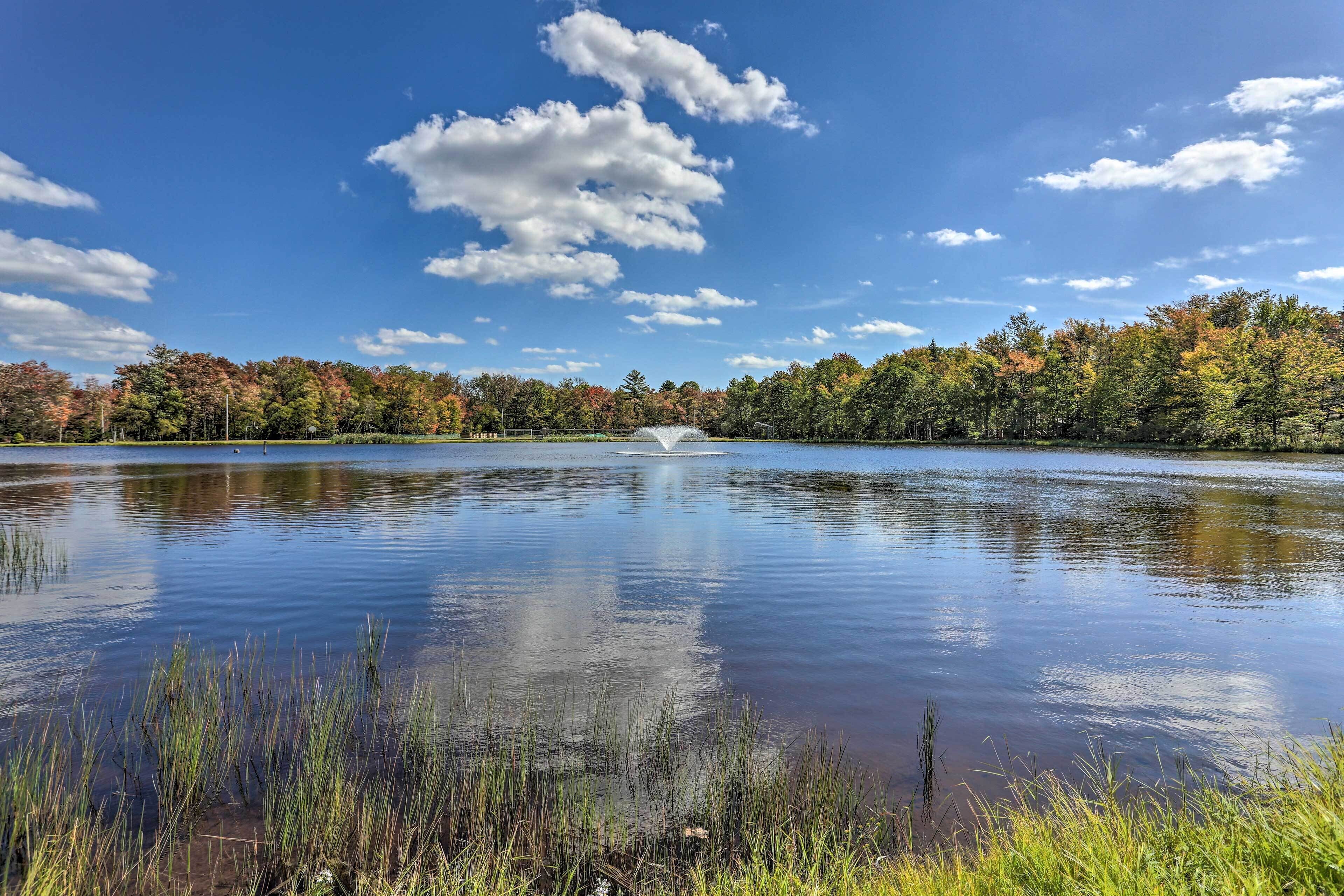 A tranquil lake with a fountain in the center, surrounded by trees with autumn foliage.