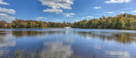 A tranquil lake with a fountain in the center, surrounded by trees with autumn foliage.