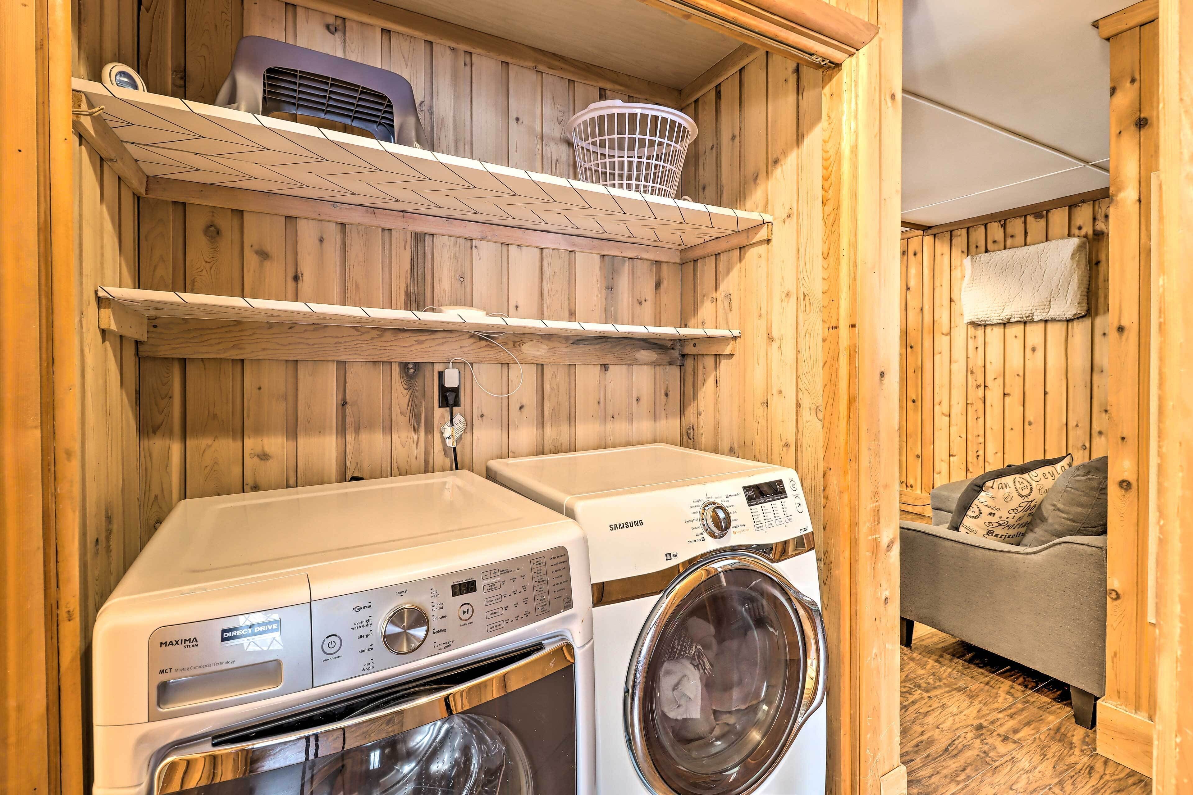 A laundry area with two washing machines, a drying rack, and a couch in a wooden room.