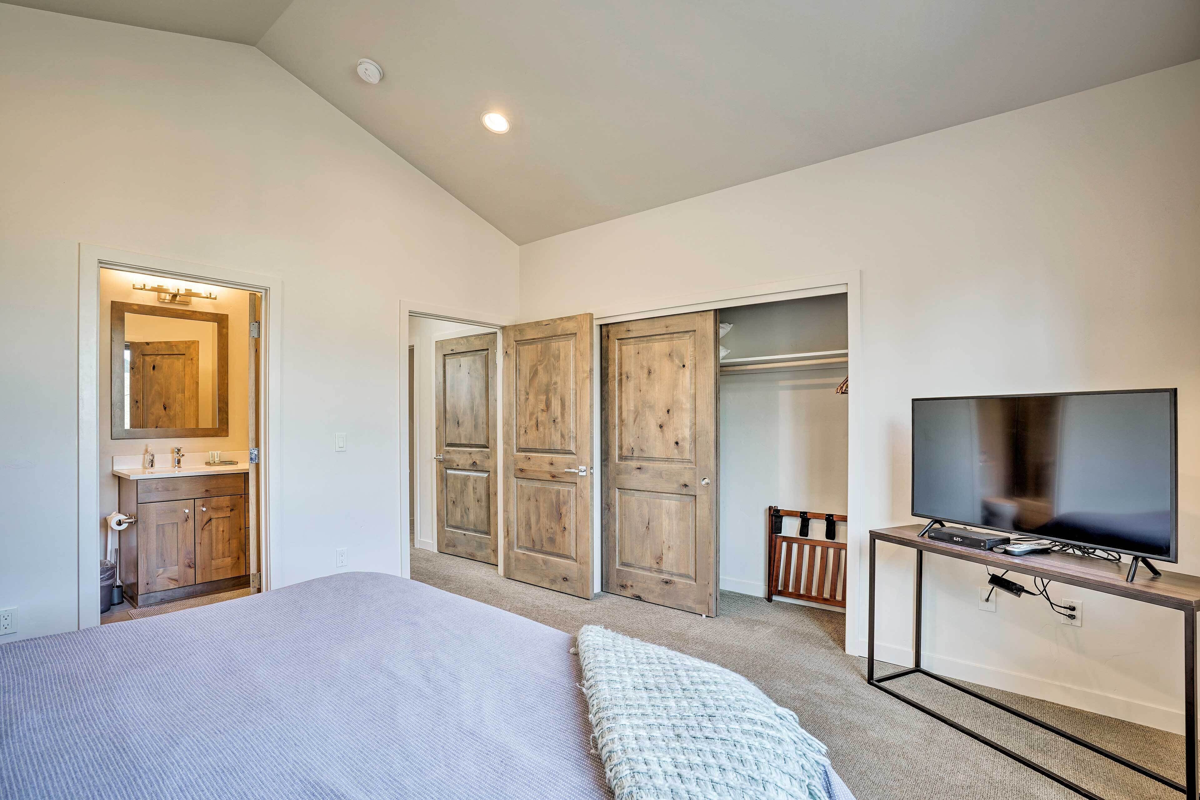 A bedroom with a bed, a TV on a stand, wooden doors, and a closet.