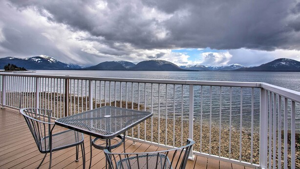 A deck with a table and chairs overlooking a lake with mountains in the background.