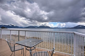 A deck with a table and chairs overlooking a lake with mountains in the background.