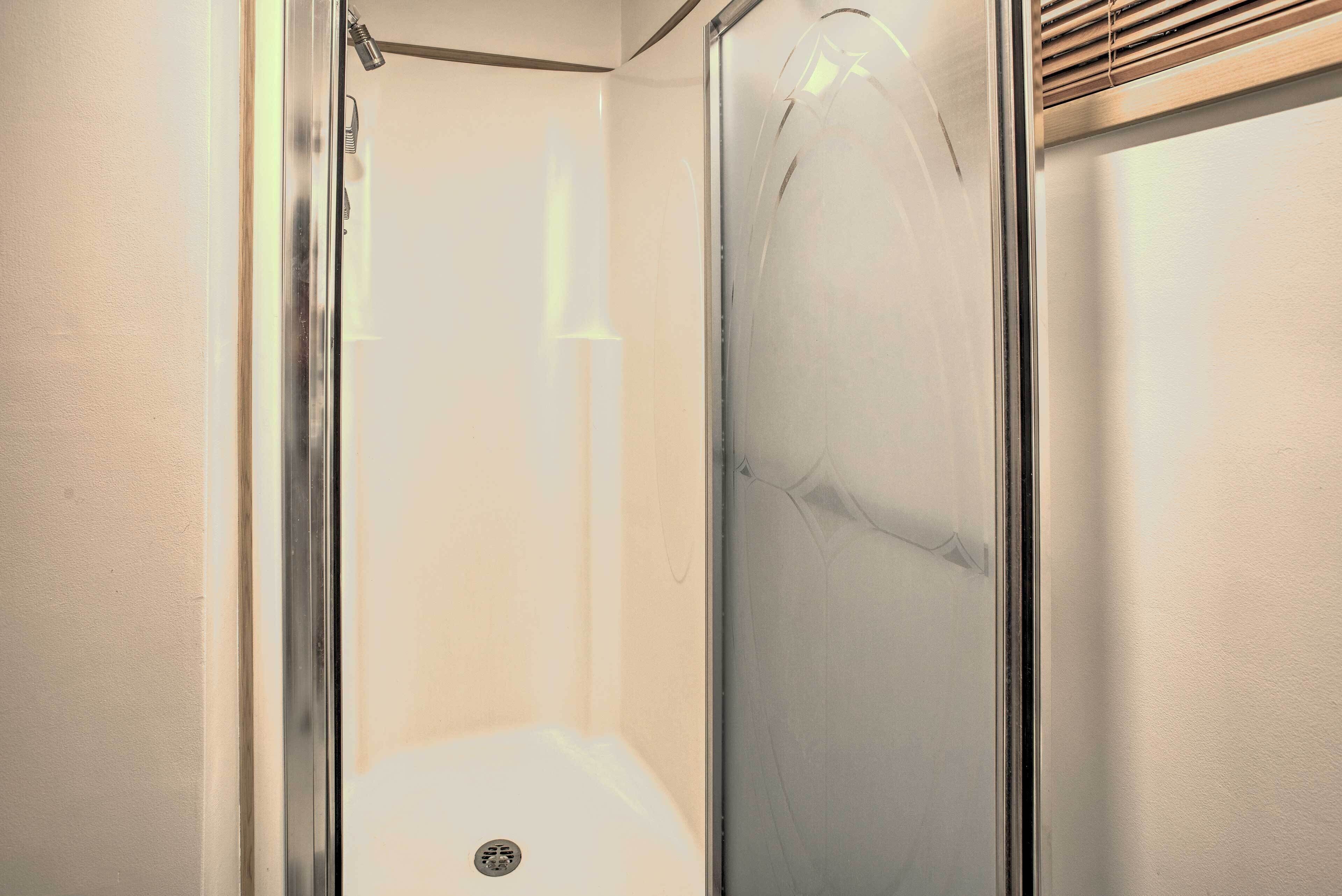 A glass-enclosed shower with a stainless steel frame, a visible drain, and a light switch on the wall.