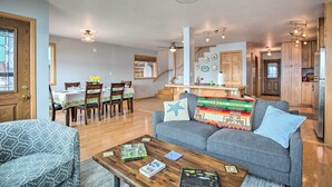 A spacious living area with a grey sofa, wooden dining table, and a staircase leading to the upper floor.