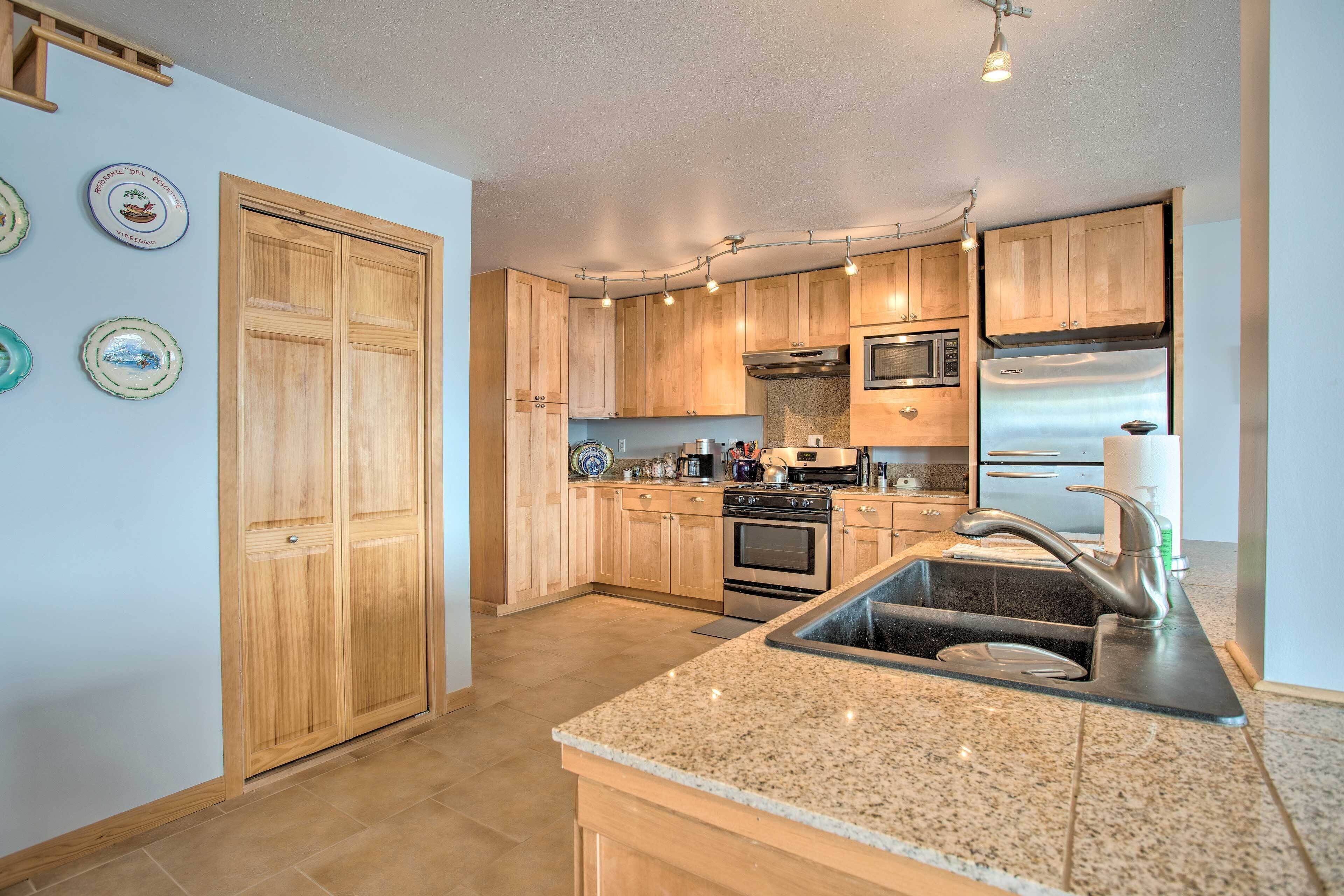 A kitchen with wooden cabinets, a stainless steel refrigerator, and a granite countertop.