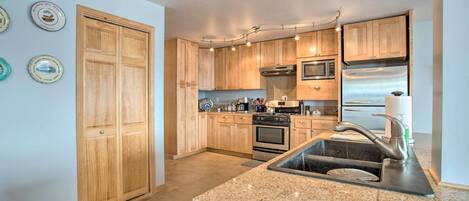 A kitchen with wooden cabinets, a stainless steel refrigerator, and a granite countertop.