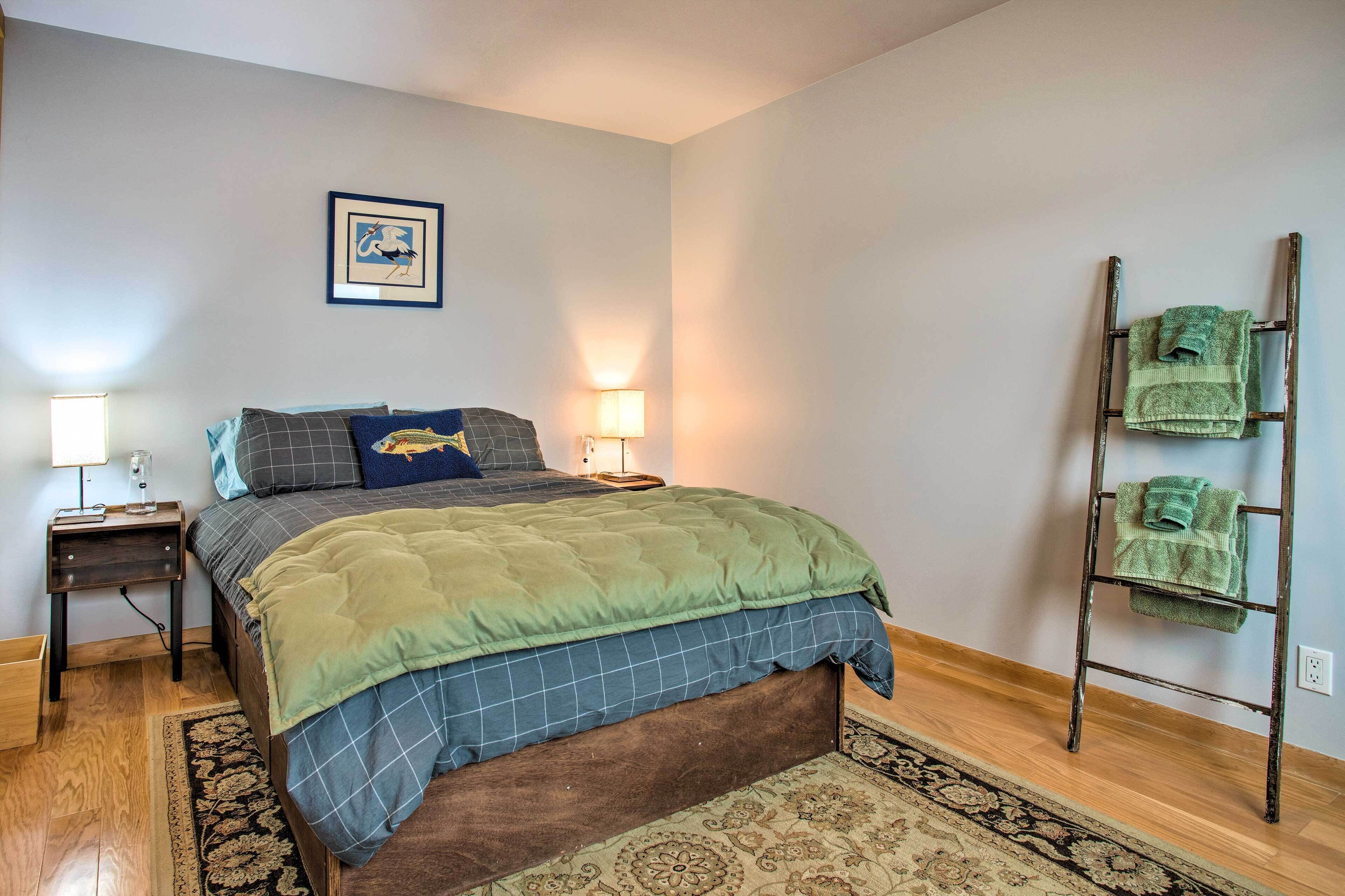A bedroom with a bed, two bedside lamps, a wall-mounted picture, and a towel rack.