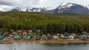 A lakeside village with houses on stilts, a forested mountain backdrop, and a clear view of the water.