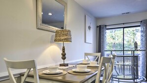 A dining area with a table set for four, a lamp, and a chair with a woven seat. - Modern Townhome w/ Deck & Golf Course Views! (Pinehurst)