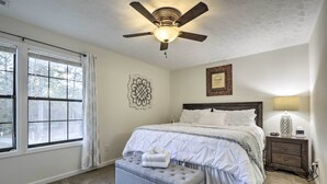 A bedroom with a bed, a nightstand, a ceiling fan, a window with curtains, and a wall decoration. - Modern Townhome w/ Deck & Golf Course Views! (Pinehurst)