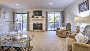 A spacious living room with a fireplace, comfortable seating, a glass coffee table, and a balcony with outdoor furniture. - Modern Townhome w/ Deck & Golf Course Views! (Pinehurst)