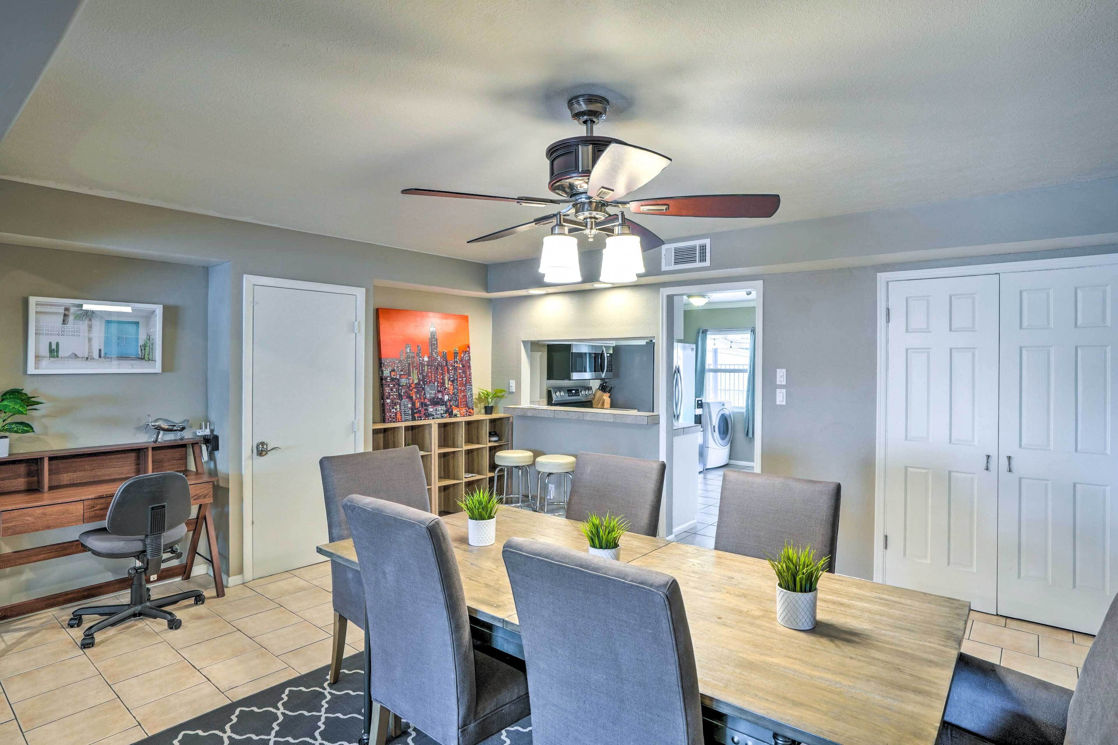 A modern dining area with a wooden table, grey chairs, and a ceiling fan.