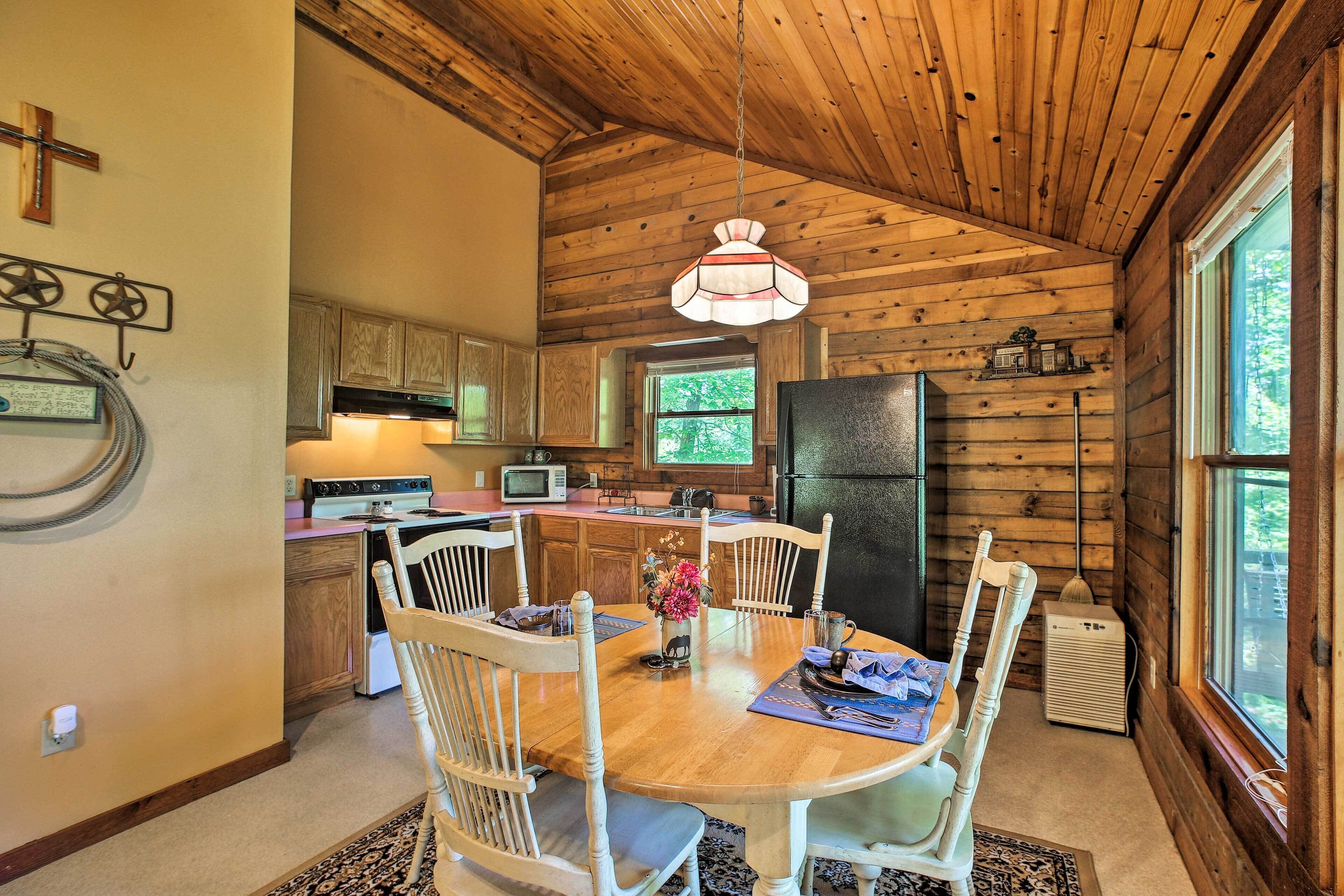 A wooden cabin kitchen with a dining table, chairs, and a hanging light fixture.