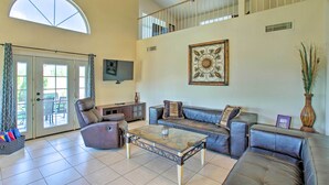A spacious living room with a high ceiling, a ceiling fan, a large window, and a fireplace. - Goodyear Home w/ Pool, Quiet Walkable Community (Goodyear)