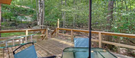 A wooden deck with glass tables and chairs, surrounded by trees.