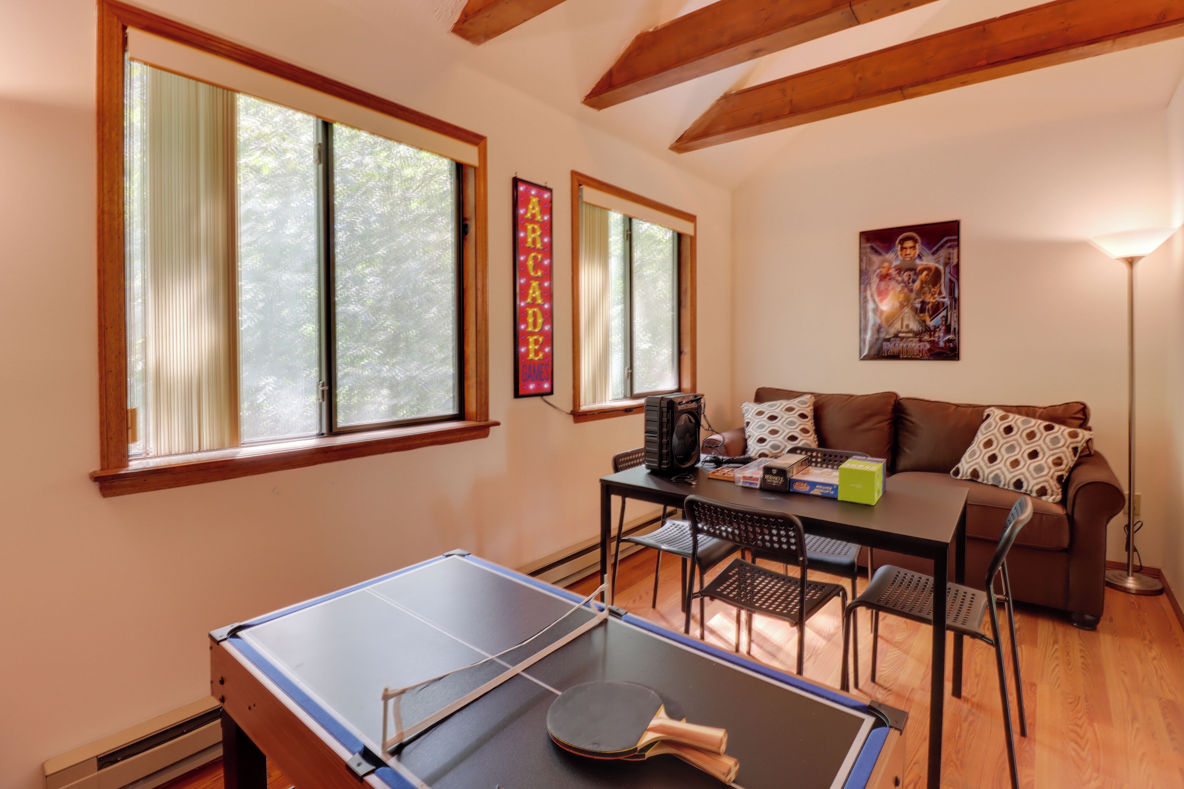 A room with a ping pong table, a couch, a coffee table, and a poster on the wall.