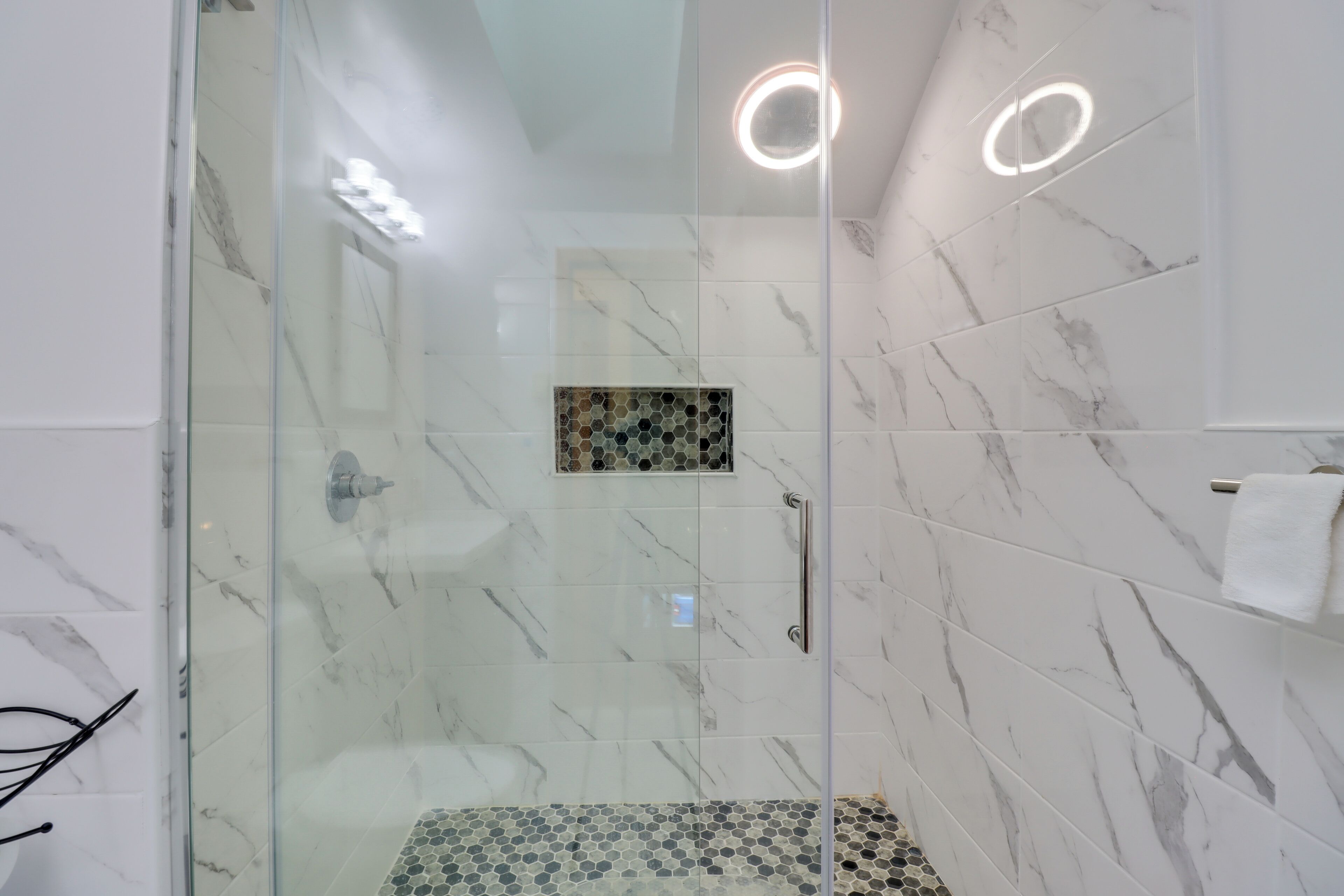 Une salle de bain moderne avec une douche à parois de verre, des carreaux de marbre et un mur décoratif en mosaïque.