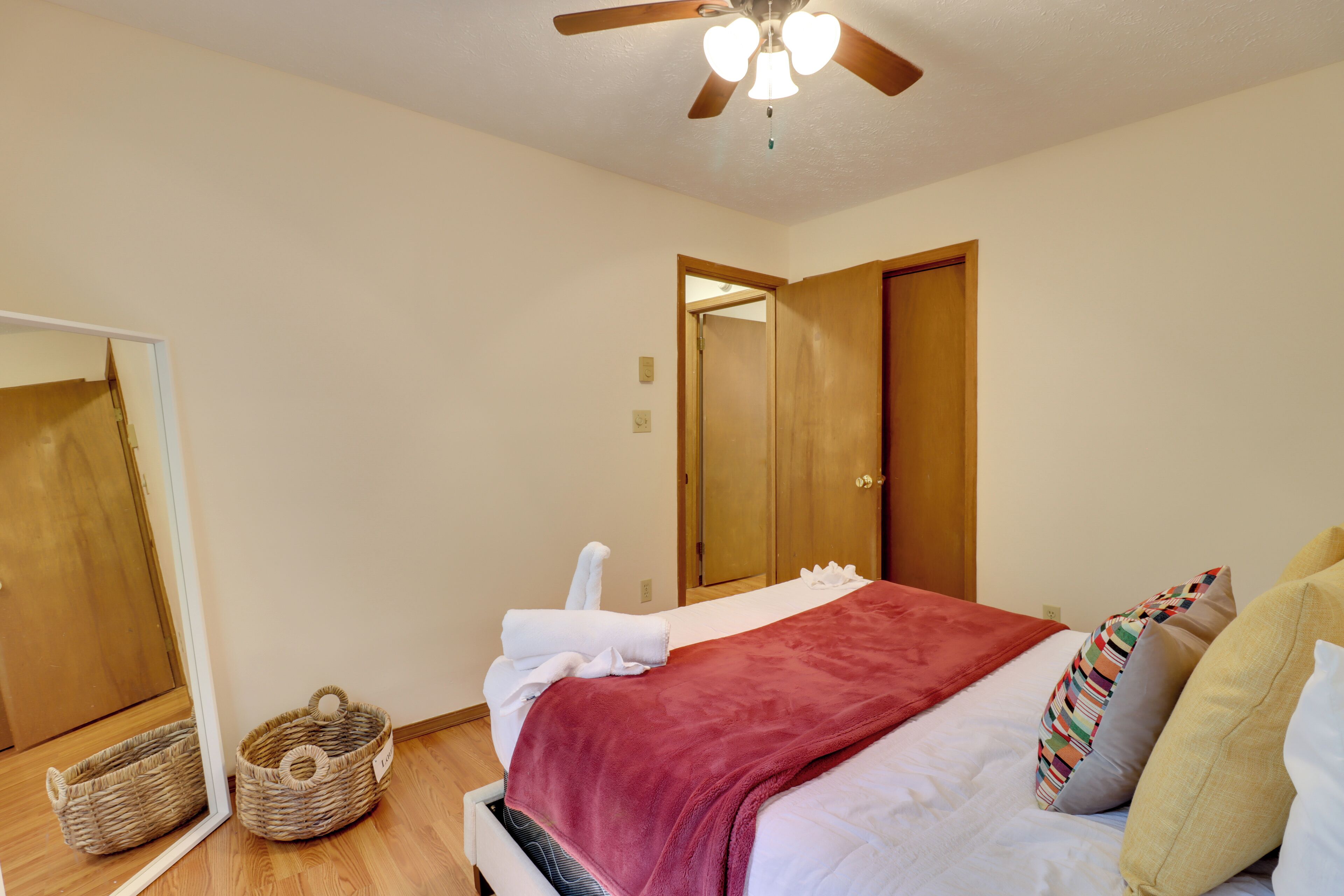 A bedroom with a bed, a ceiling fan, a mirror, a wooden door, and a small wicker basket.