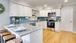 A modern kitchen with white cabinets, a granite countertop, a built-in oven, and a microwave. - Sunsets, Salt Air and Single-story Ease in Fenwick (Selbyville)