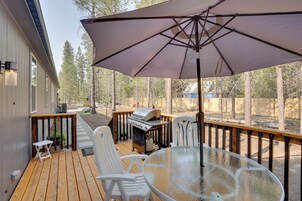 A wooden deck with a grill, white chairs, and a glass table under a large umbrella.
