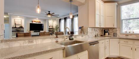 A modern kitchen with white cabinets, granite countertops, stainless steel appliances, and pendant lighting.