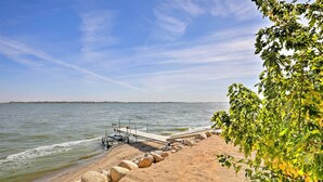A beach with a wooden pier extending into calm waters, surrounded by a rocky shoreline and lush greenery. - Private Sauna, Hot Tub, Beach Lake Poinsett (Lake Norden)