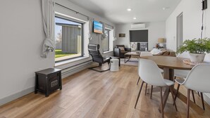 A modern, well-lit room with a large window, a television, a desk, and a dining area with chairs. - Private Sauna, Hot Tub, Beach Lake Poinsett (Lake Norden)